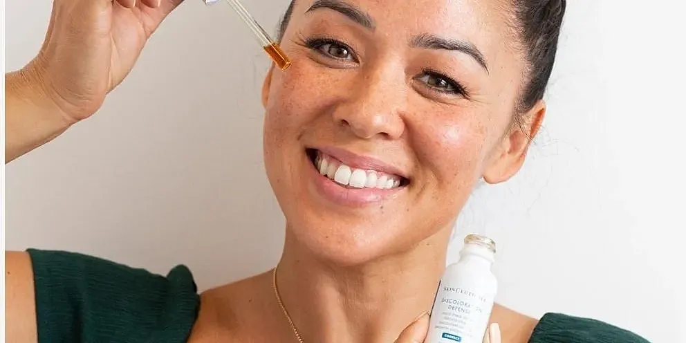 Smiling woman applying skincare serum.