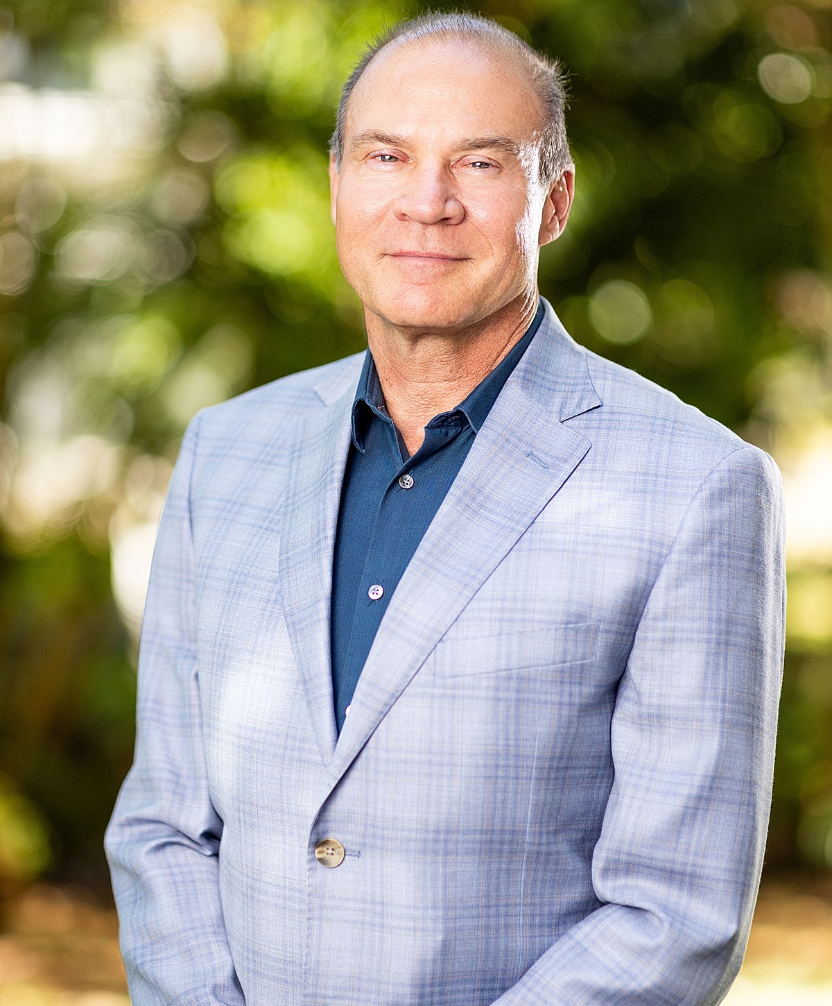 Man in blazer smiling outdoors with blurred background