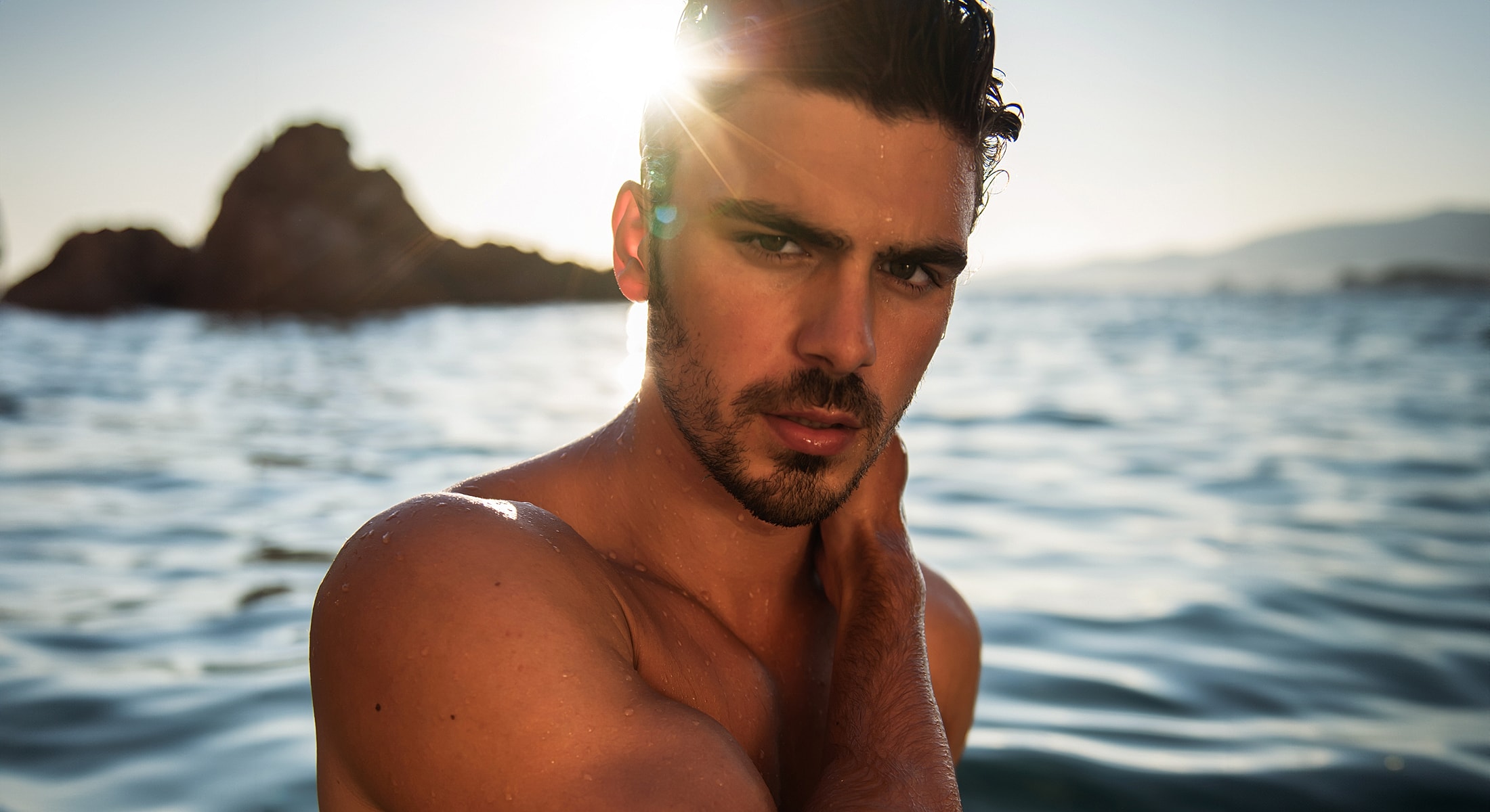 Man by water with sun rays shining behind.